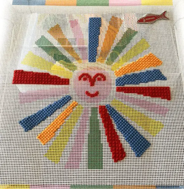 A sunface needlepoint canvas designed by Thread Bear Kits is shown in progress.