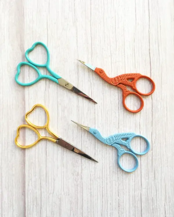 Four pairs of colourful embroidery scissors sit on top of a wooden background.
