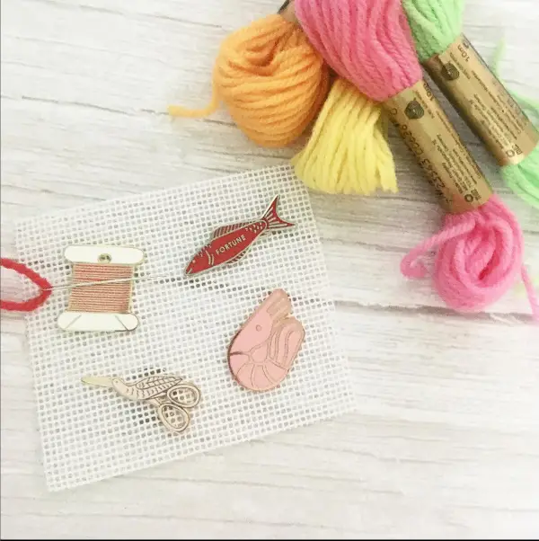 Four magnetic and enamel needle minders are sandwiched on some needlepoint canvas.