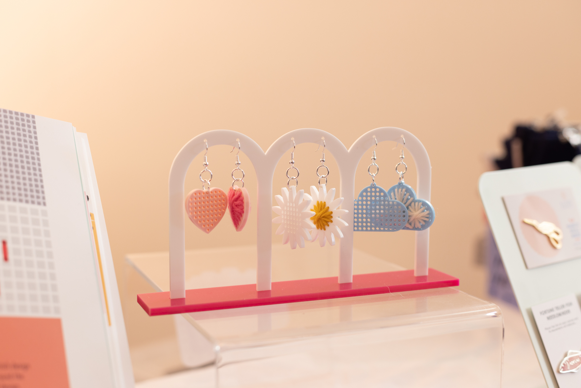 Acrylic earrings with stitchable middles hang from a display stand.