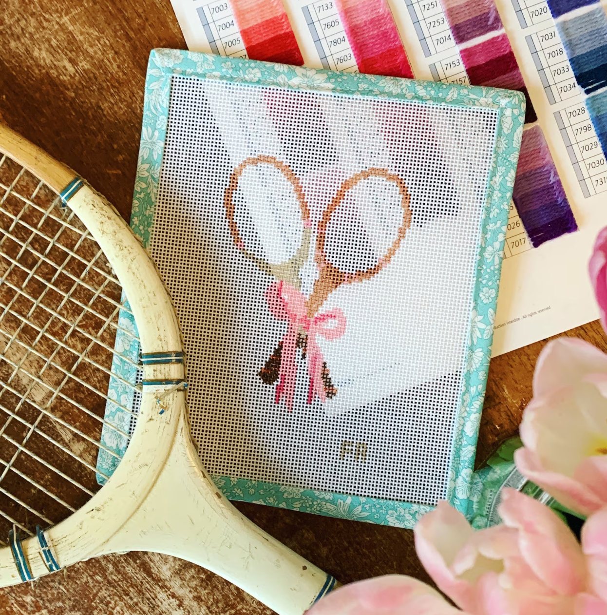 A styled scene shows a hand painted needlepoint canvas picture pair of tennis rackets.